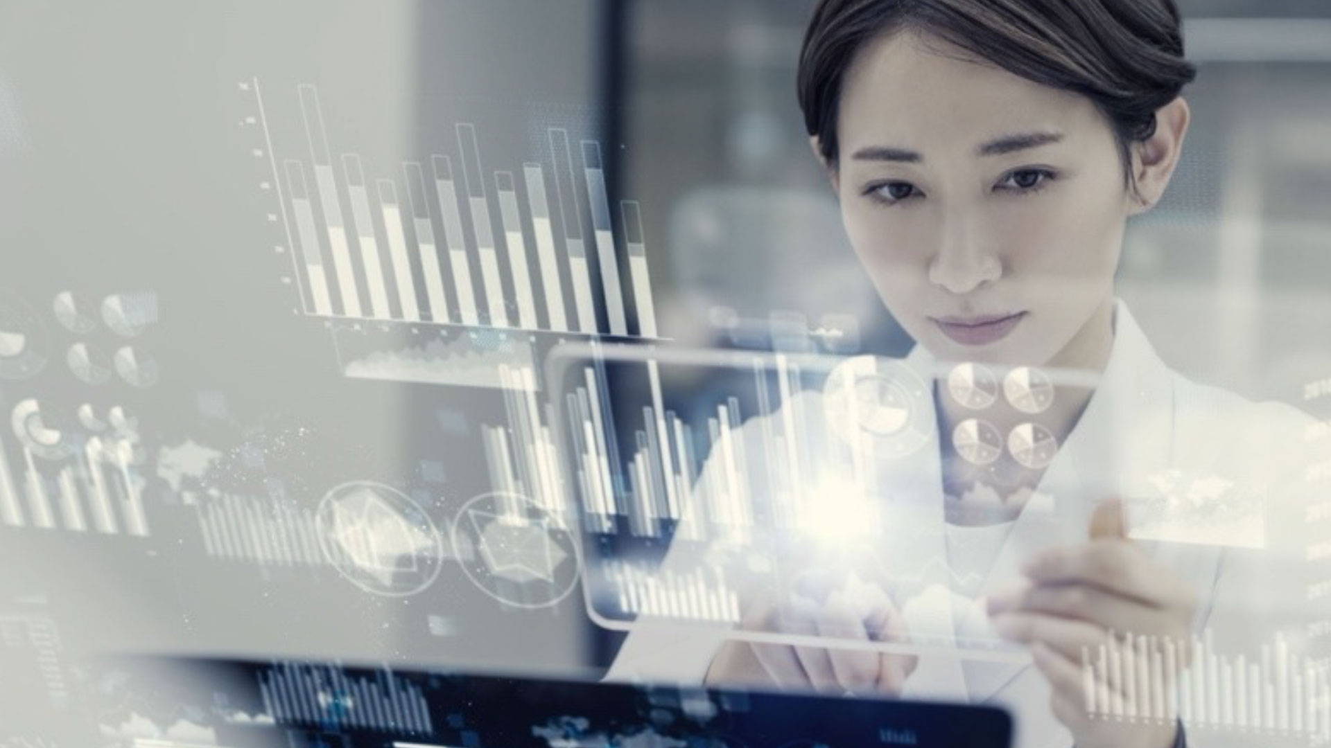 A woman wearing a lab coat interacting with digital projections of and infographics above a computer screen